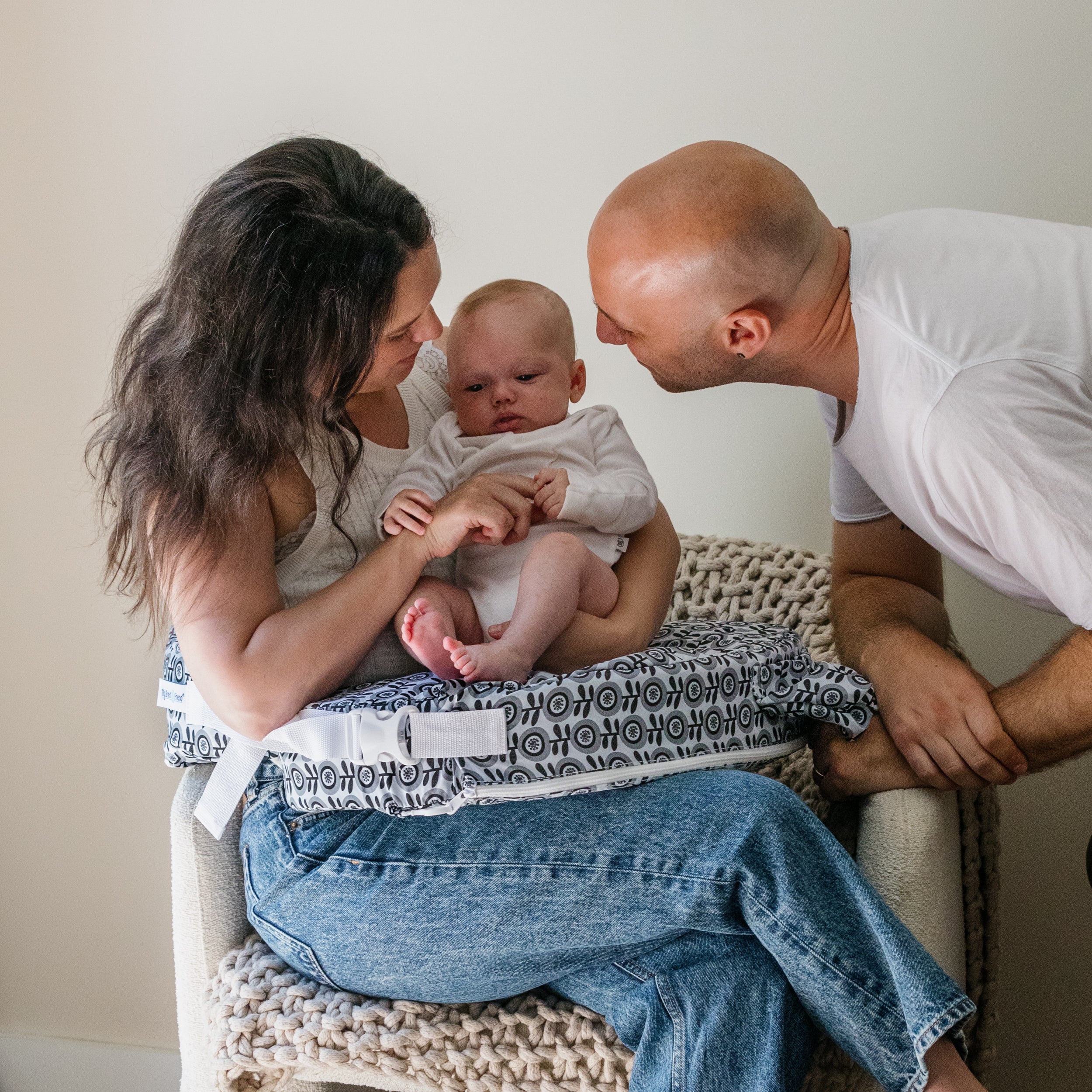 Family of three sitting together on a chair with a neutral background