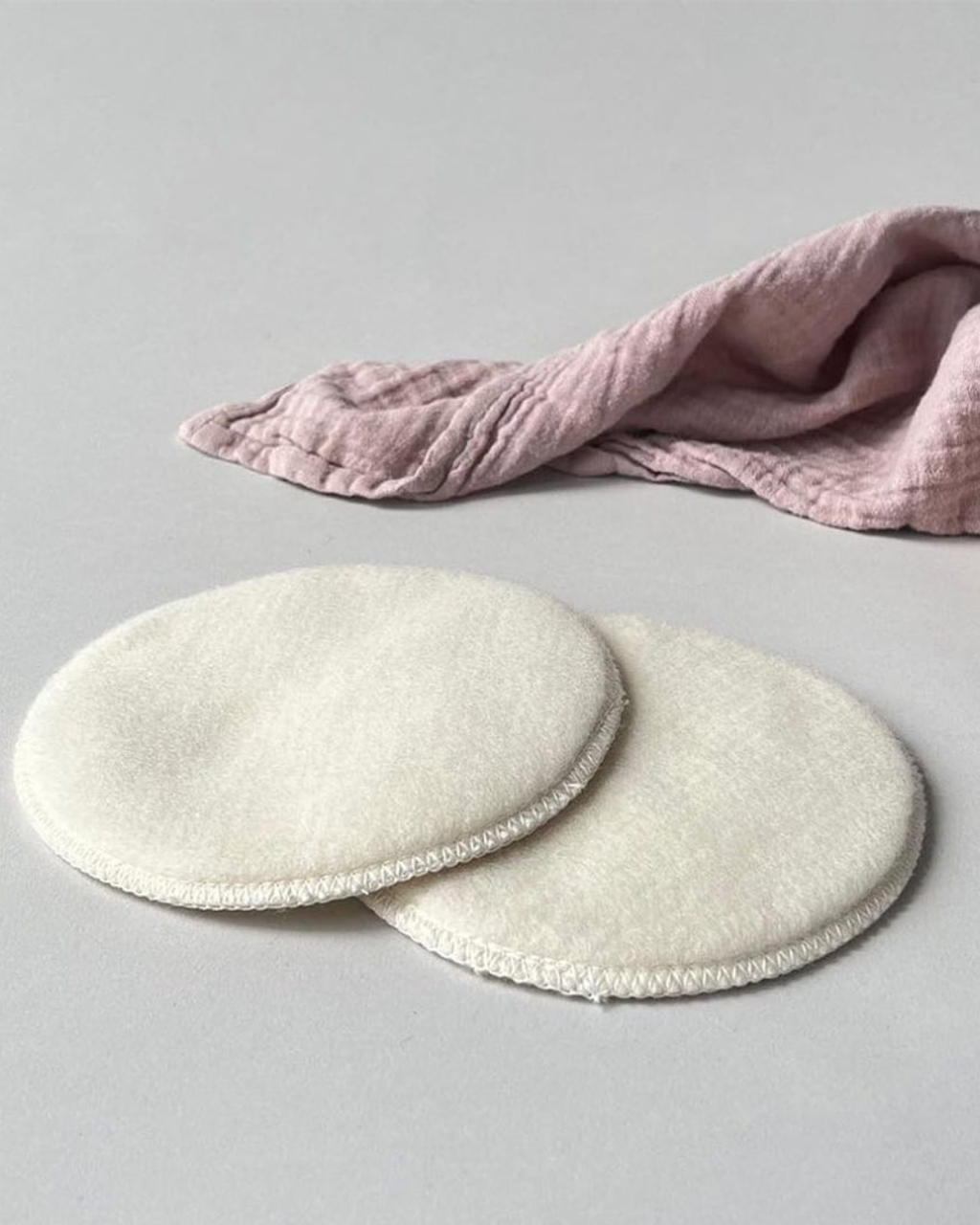 Two white circular pads on a gray surface with a pink cloth in the background.