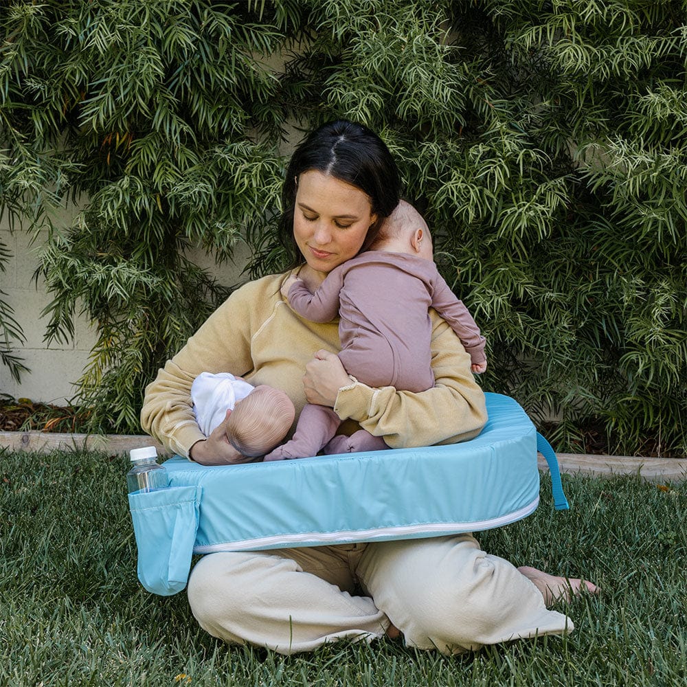 Woman holding a baby on a portable changing table outdoors.