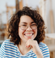 Woman with glasses and curly hair wearing a striped shirt, smiling.