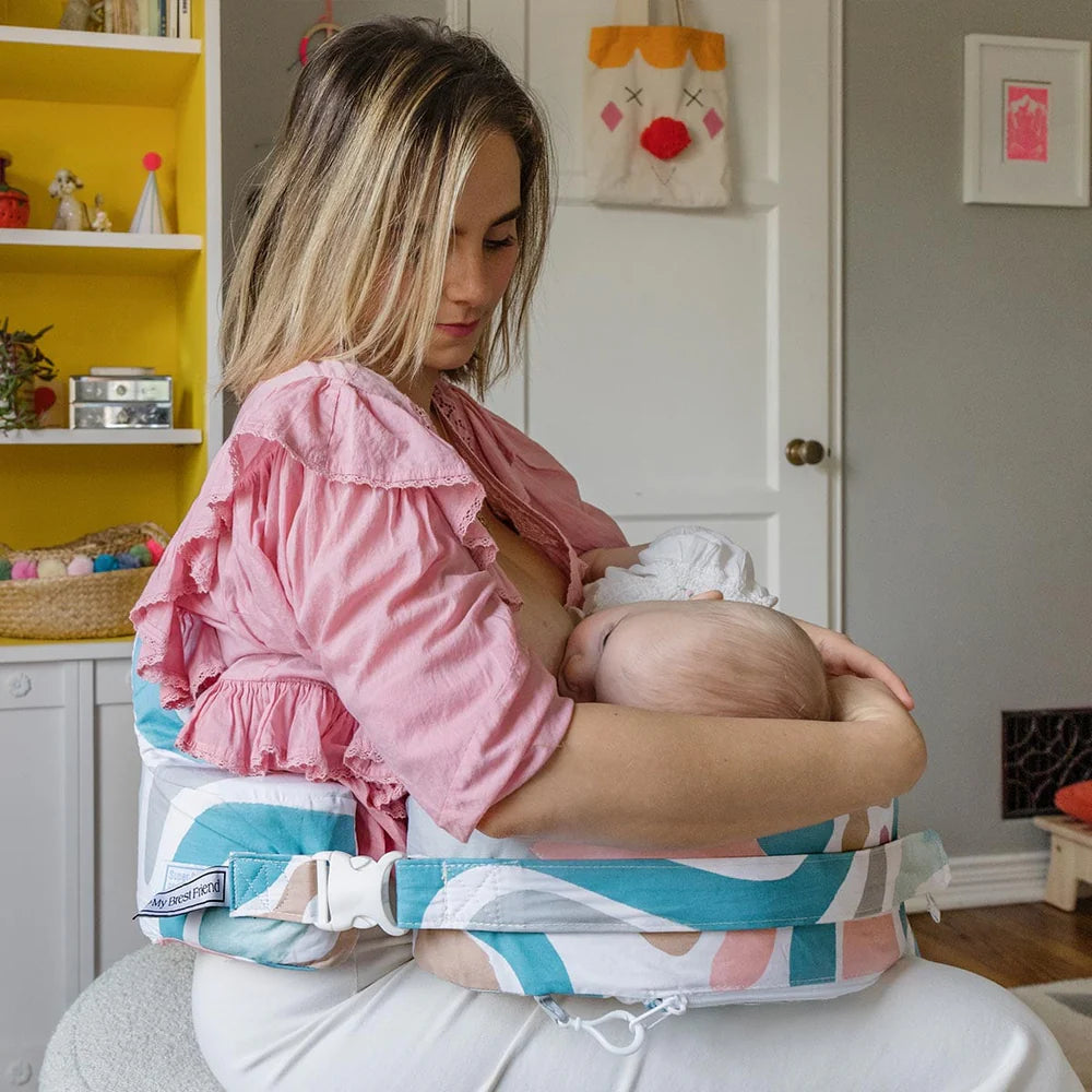 Woman holding a baby in a colorful carrier in a home setting
