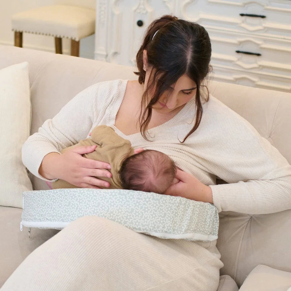 Woman breastfeeding a baby using a nursing pillow on a couch.