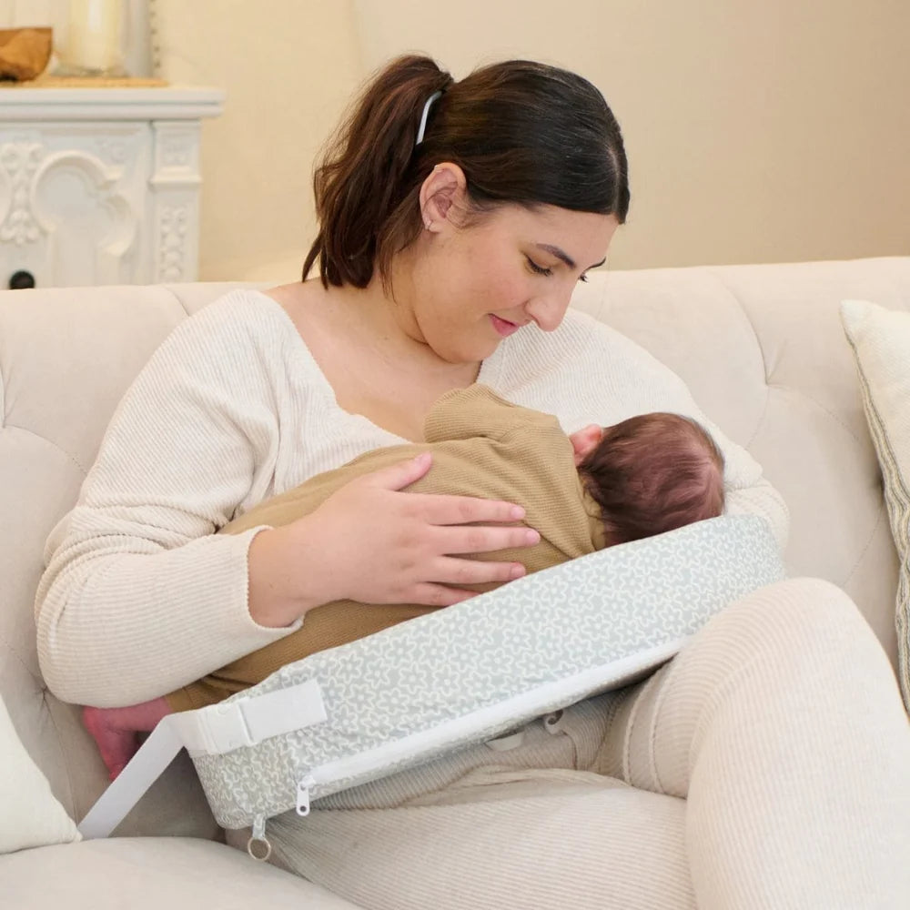 Woman breastfeeding a baby using a specialized support device on a couch.