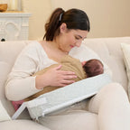 Woman breastfeeding a baby using a specialized support device on a couch.