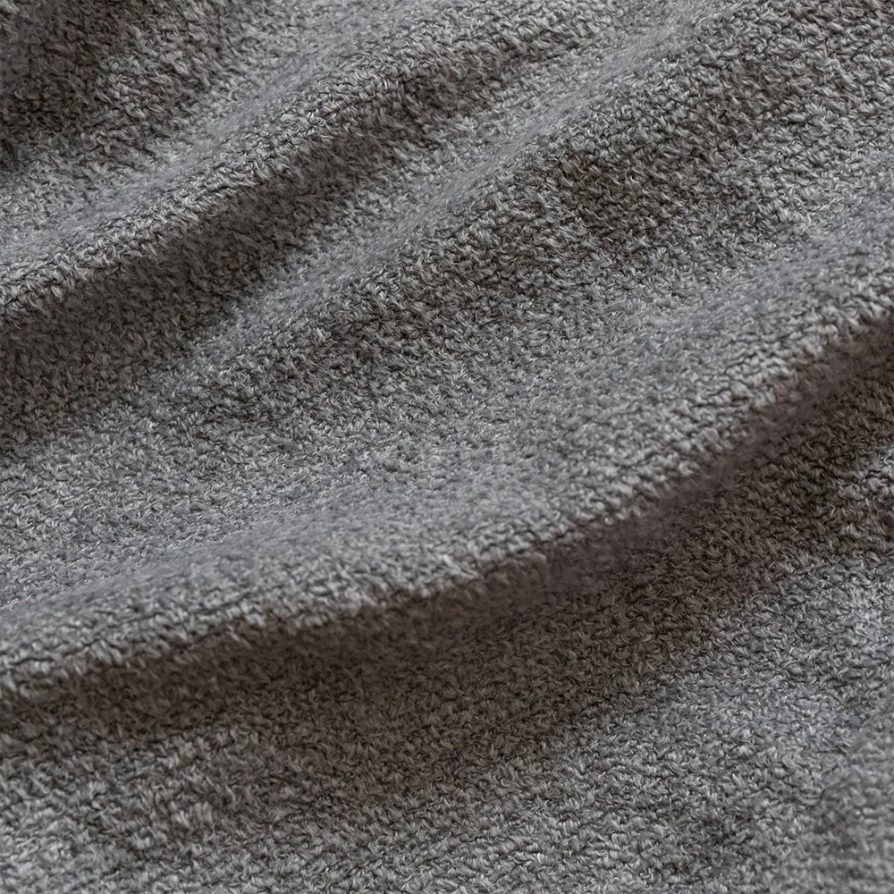 Close-up of textured gray fabric with a soft, looped surface. The light and shadows highlight its wavy, plush appearance, conveying a sense of warmth.