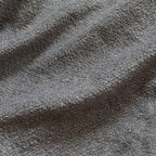 Close-up of textured gray fabric with a soft, looped surface. The light and shadows highlight its wavy, plush appearance, conveying a sense of warmth.
