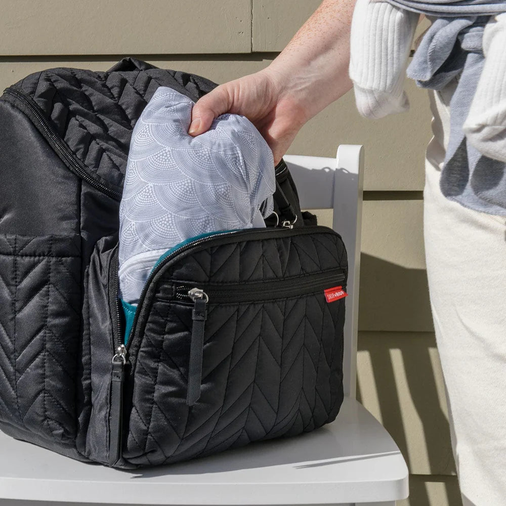 Person packing a quilted black backpack with a gray garment