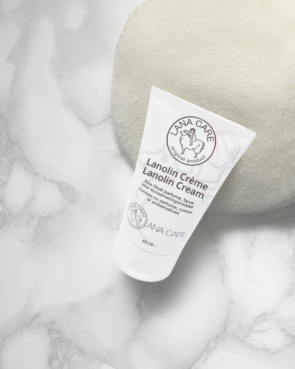 Plastic tube of Lanolin Creme by LANACare sits on beige fabric. The label features a circular sheep logo. The scene conveys a sense of softness.