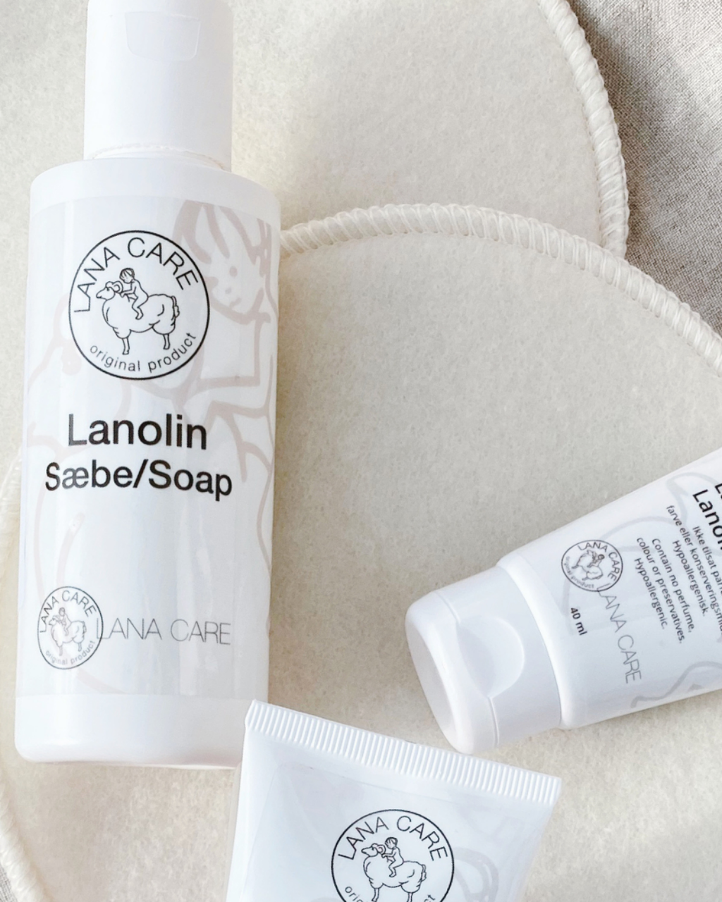 Close-up of LANACare lanolin soap and cream tubes on soft, beige pads. Clean, minimalist packaging with a calming, natural feel.