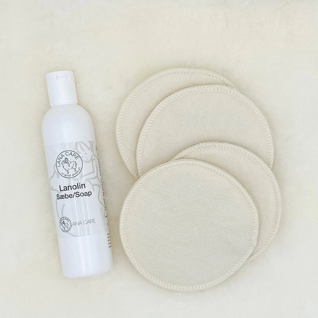 White bottle of Lanolin Soap with four round white pads on a beige background