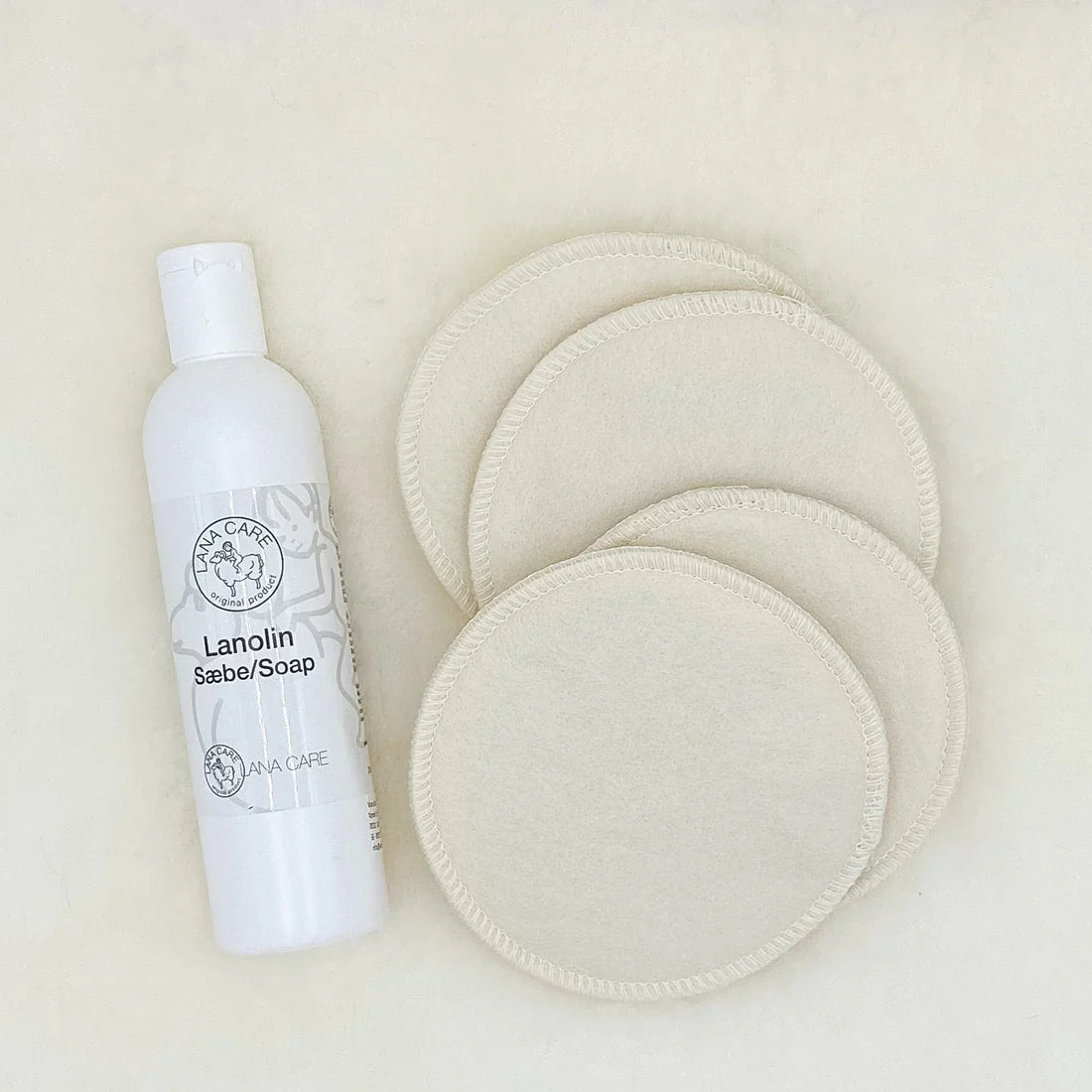 White bottle of lanolin soap with round white wool nursing pads on a beige background