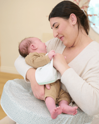 Woman breastfeeding a baby using a nursing pillow in a home setting.