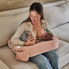 Woman breastfeeding twins using a pink哺乳枕 on a couch.