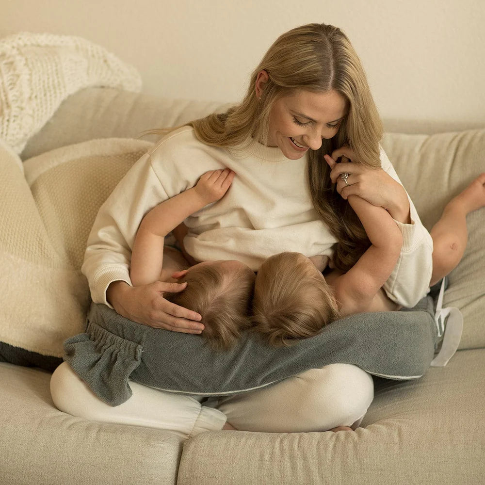 Woman sitting on a couch holding two children close to her chest.