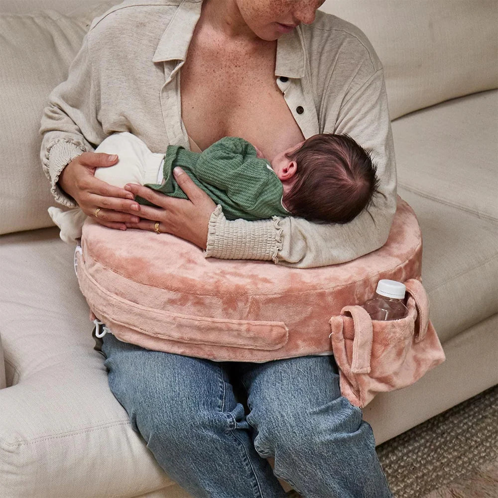 Person breastfeeding a baby using a pink nursing pillow on a couch.