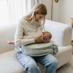 Woman breastfeeding a baby using a nursing pillow in a cozy room.