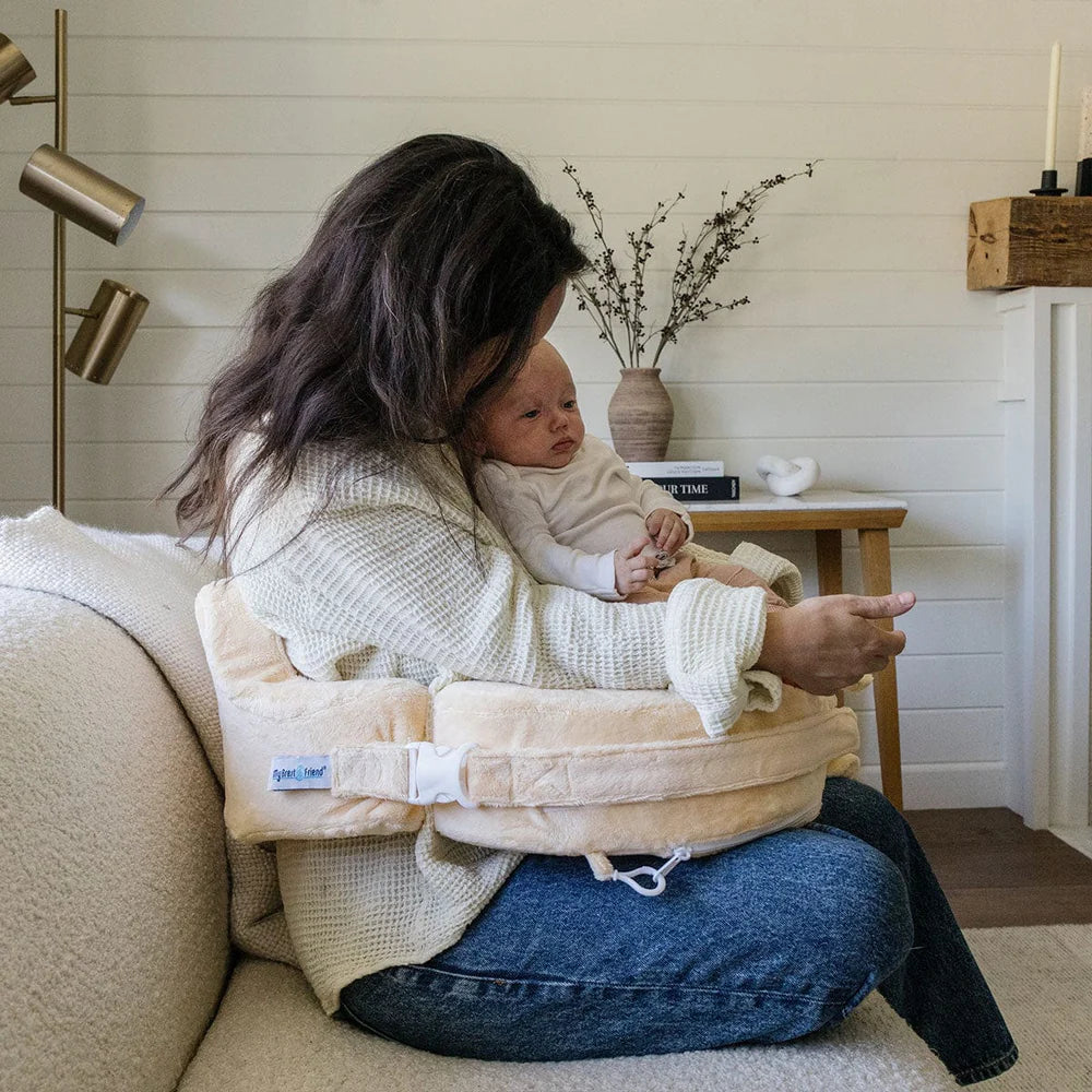 Woman holding a baby in a carrier on a couch in a cozy living room.
